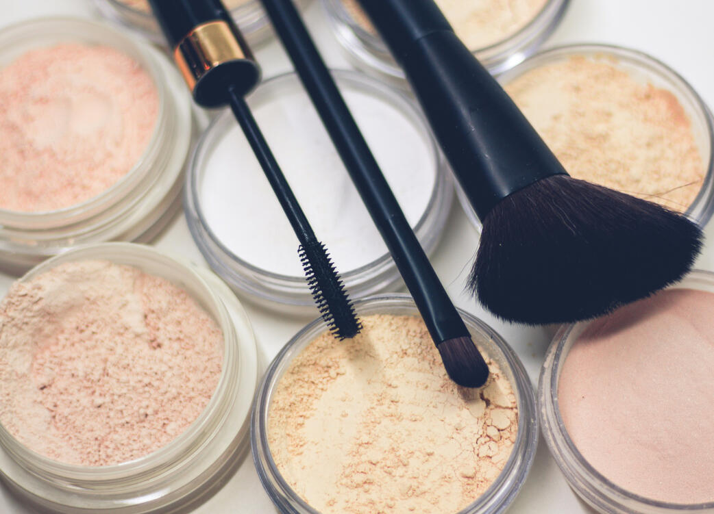 Makeup brushes, mascara wand, and loose setting powder jars arranged on a white surface for a clean beauty routine